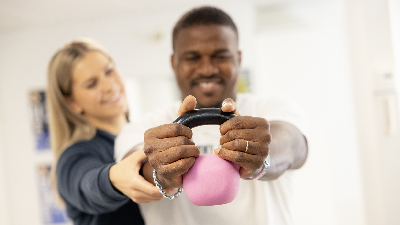 a pink kettle bell, held by hands of two smiling people out of focus at the backround