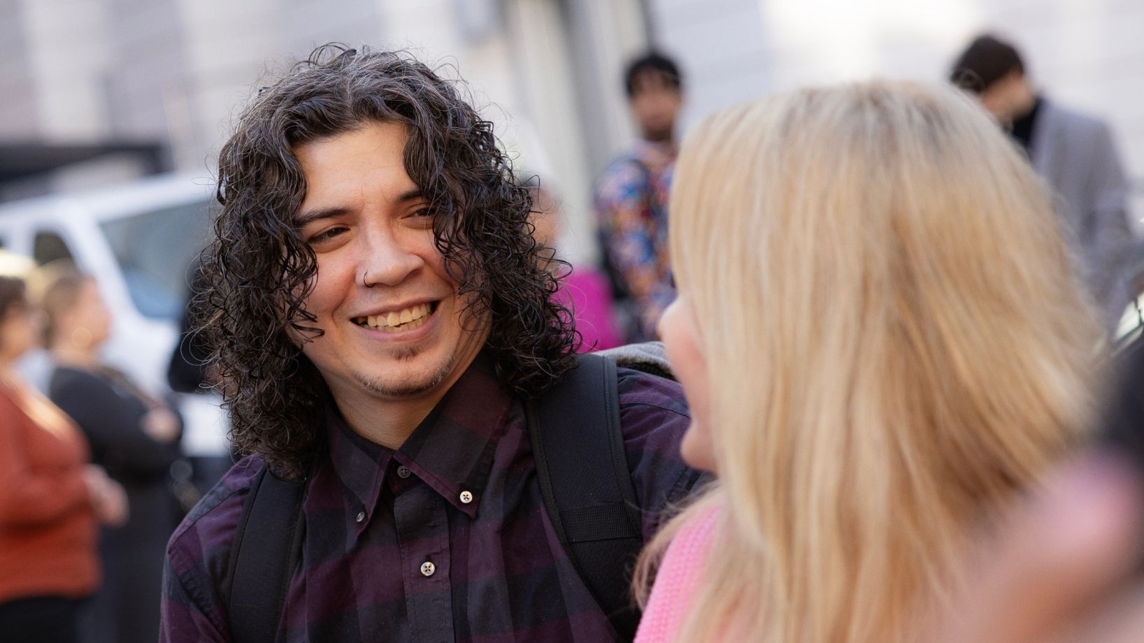 a man with long black curly hair smiling at someone with long blond wavy hair