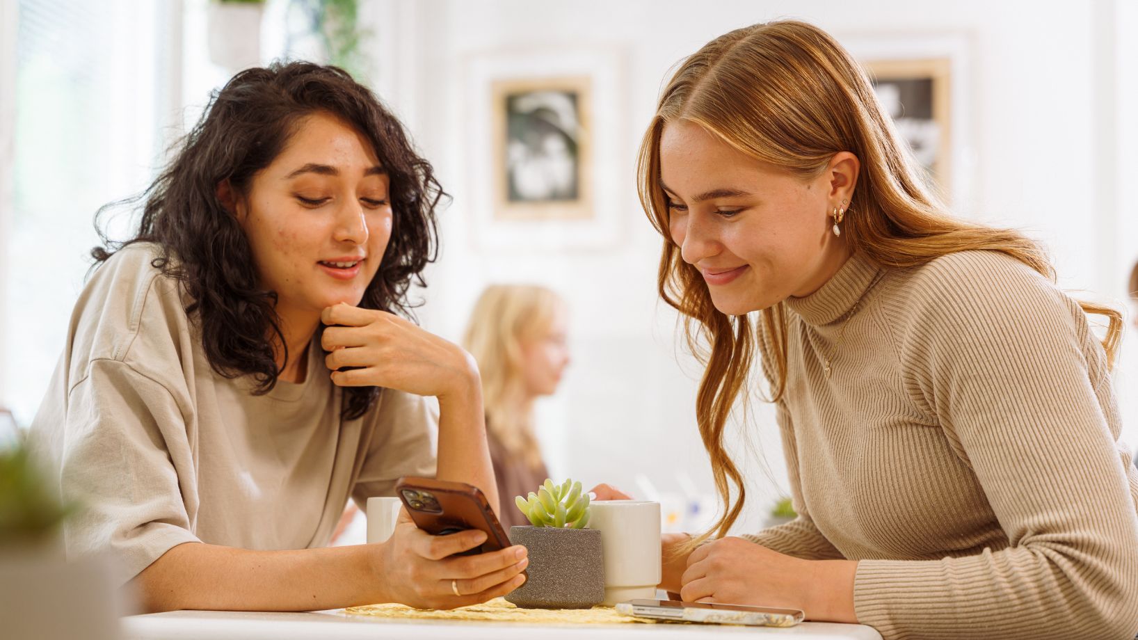two young women sitting at a table looking at something on a phone screen