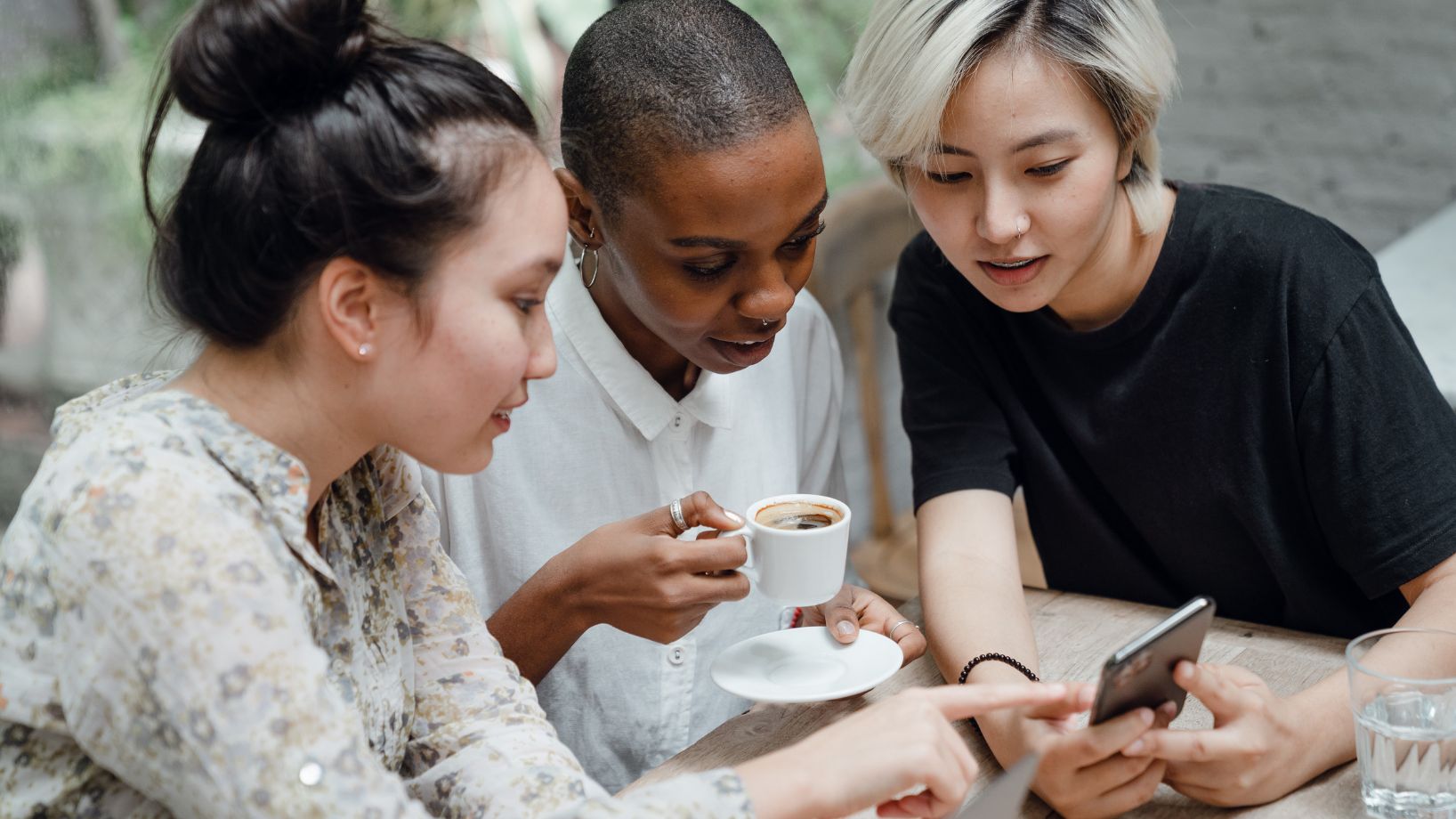 three young people sitting at a table with coffee and looking something on a phone